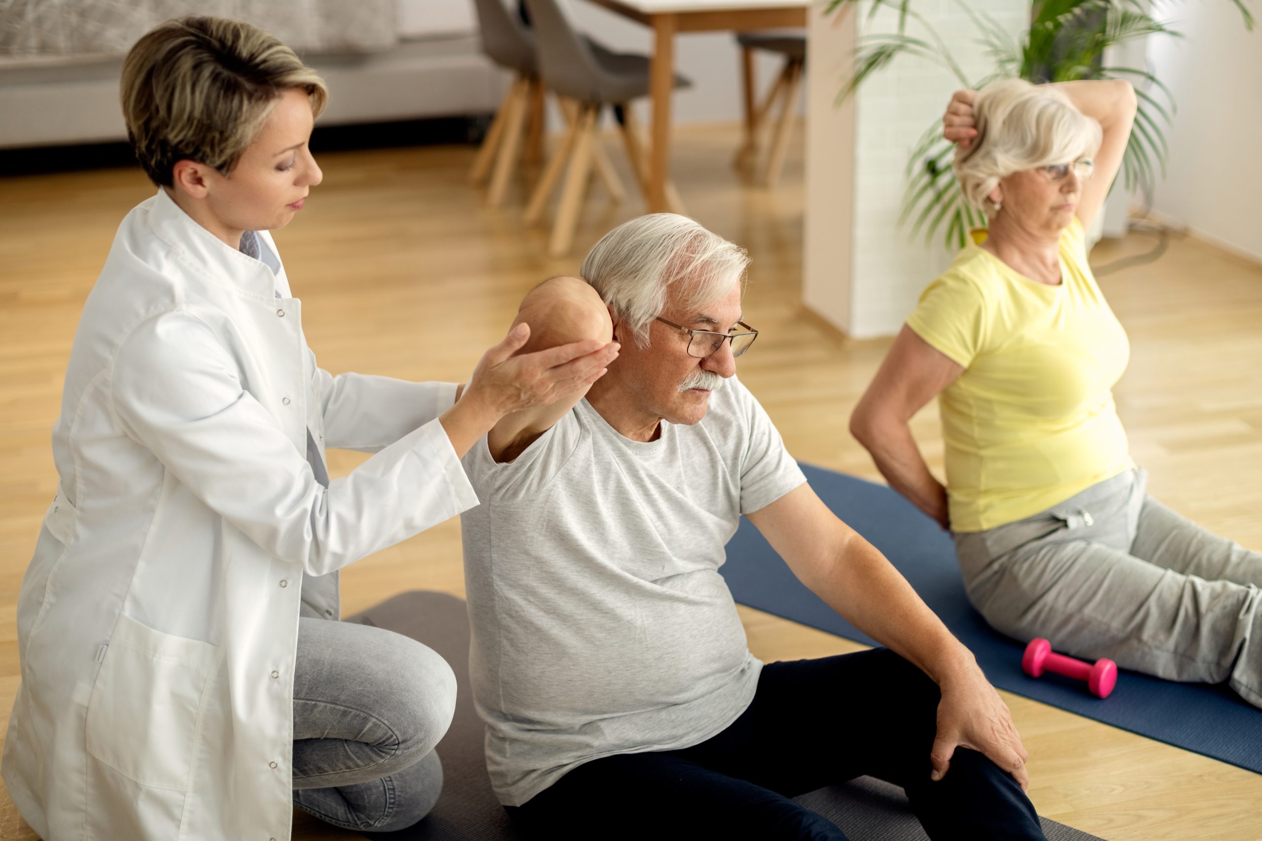 Female physiotherapist helping to senior couple with exercising at home.